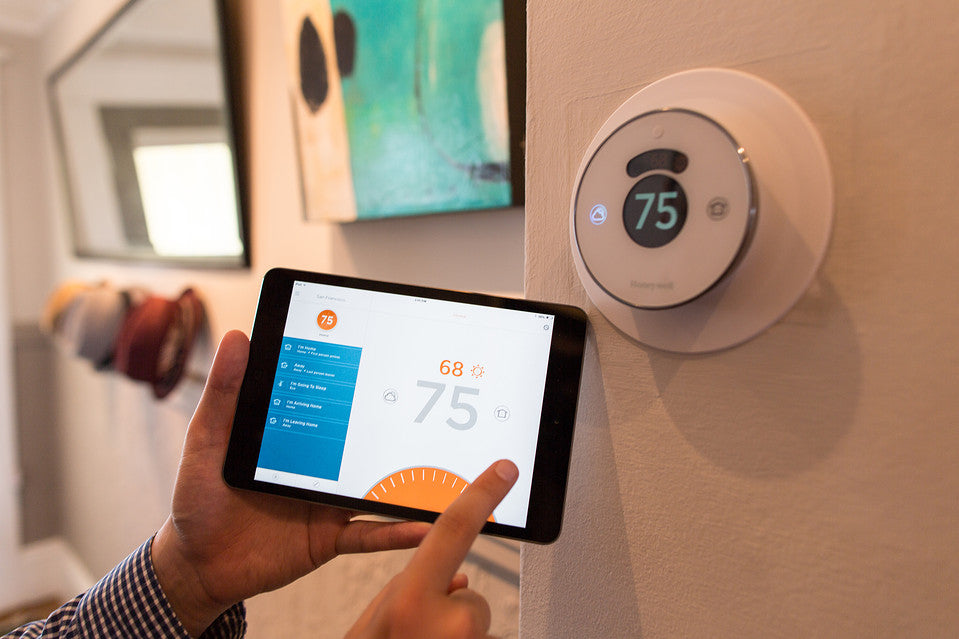Person using a tablet to control a smart thermostat on a wall, adjusting the home temperature to 75 degrees, demonstrating the convenience and precision of smart climate control systems in a modern home.